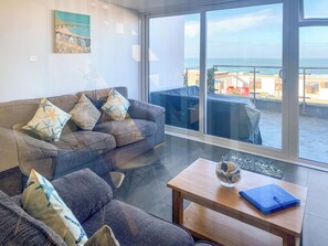 A living room with a sofa, a coffee table, and a view of the sea through large windows.