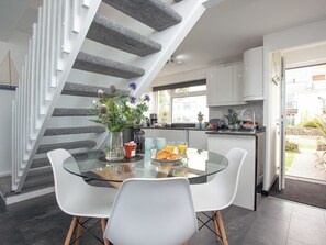 A modern kitchen with a glass dining table, white chairs, and a staircase with grey steps.