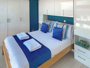 A neatly made bed with white and blue bedding, a wooden headboard, and a white nightstand with drawers. - 2 bedroom accommodation in Newquay (Newquay)