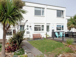 A two-story white building with a front porch, a bench, and two outdoor chairs.
