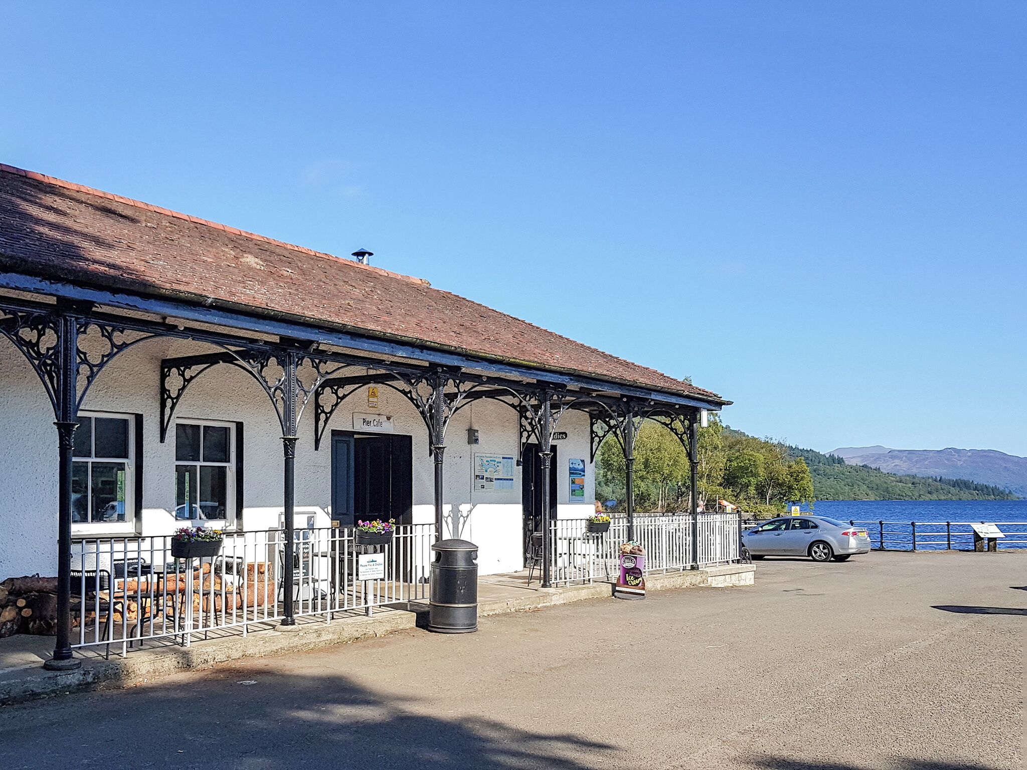 A pier cafe with a covered seating area, a trash bin, and a parked car.
