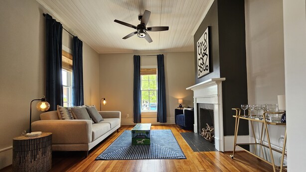 A living room with a sofa, coffee table, fireplace, and a ceiling fan. - Remodeled historic home! Steps away from dining & shops - Easy walk to Old Salem (Winston-Salem)
