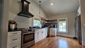 A modern kitchen with a large stove, oven, and microwave. There are wooden cabinets and a black range hood. - Remodeled historic home! Steps away from dining & shops - Easy walk to Old Salem (Winston-Salem)