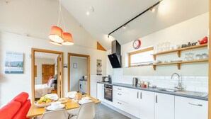Una cocina moderna con armarios blancos, un comedor con mesa y sillas de madera, y un sofá rojo.