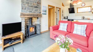 Una sala de estar con chimenea de piedra, un sofá rojo, un televisor y una cocina al fondo.
