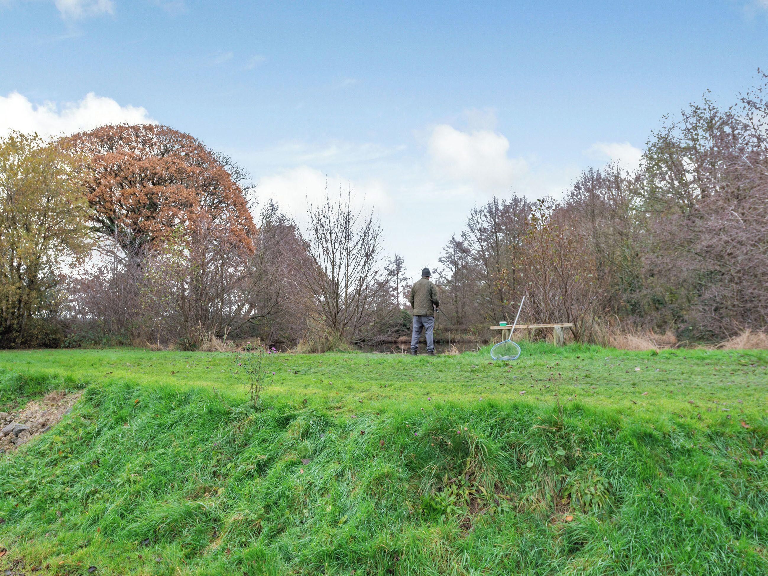 A person fishing in a grassy field with trees in the background.