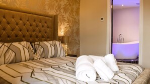 A hotel room with a large bed, a headboard, a nightstand, a lamp, and a bathroom visible through an open door.