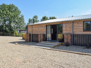 A modern log cabin with a gravel driveway, wooden steps, and a large window.