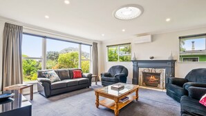 A spacious living room with a fireplace, large windows, and a view of greenery.