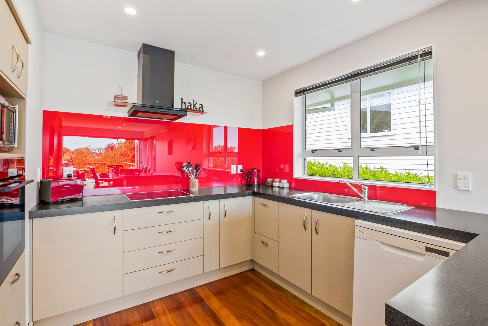 Una cocina moderna con armarios blancos, una campana extractora negra y una ventana con vistas a vegetación.