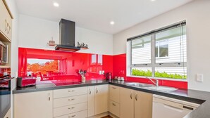 A modern kitchen with white cabinets, a black range hood, and a window with a view of greenery.