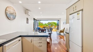 A modern kitchen with a built-in dishwasher, a large clock, and a dining area with a wooden table and chairs.