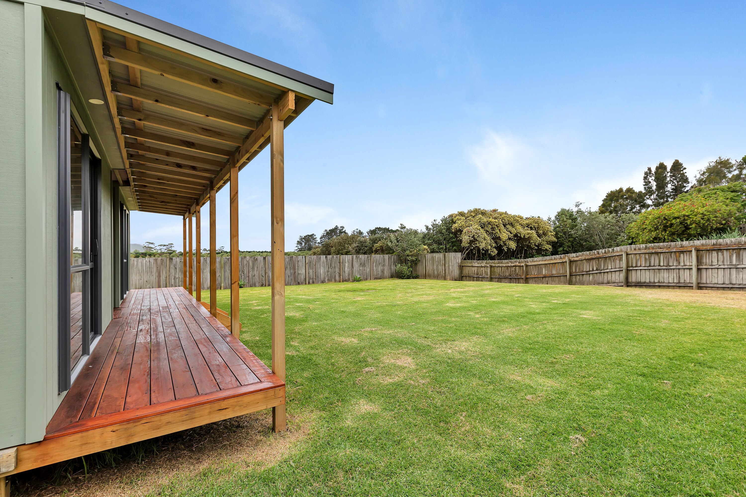 A covered patio area with a wooden deck, adjacent to a building with large windows.