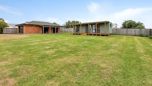 Un patio trasero residencial con una casa de ladrillo, una terraza de madera y una casa móvil verde.