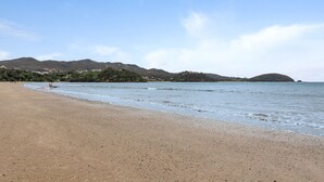 Una playa con cielo despejado, mar tranquilo y colinas a lo lejos.