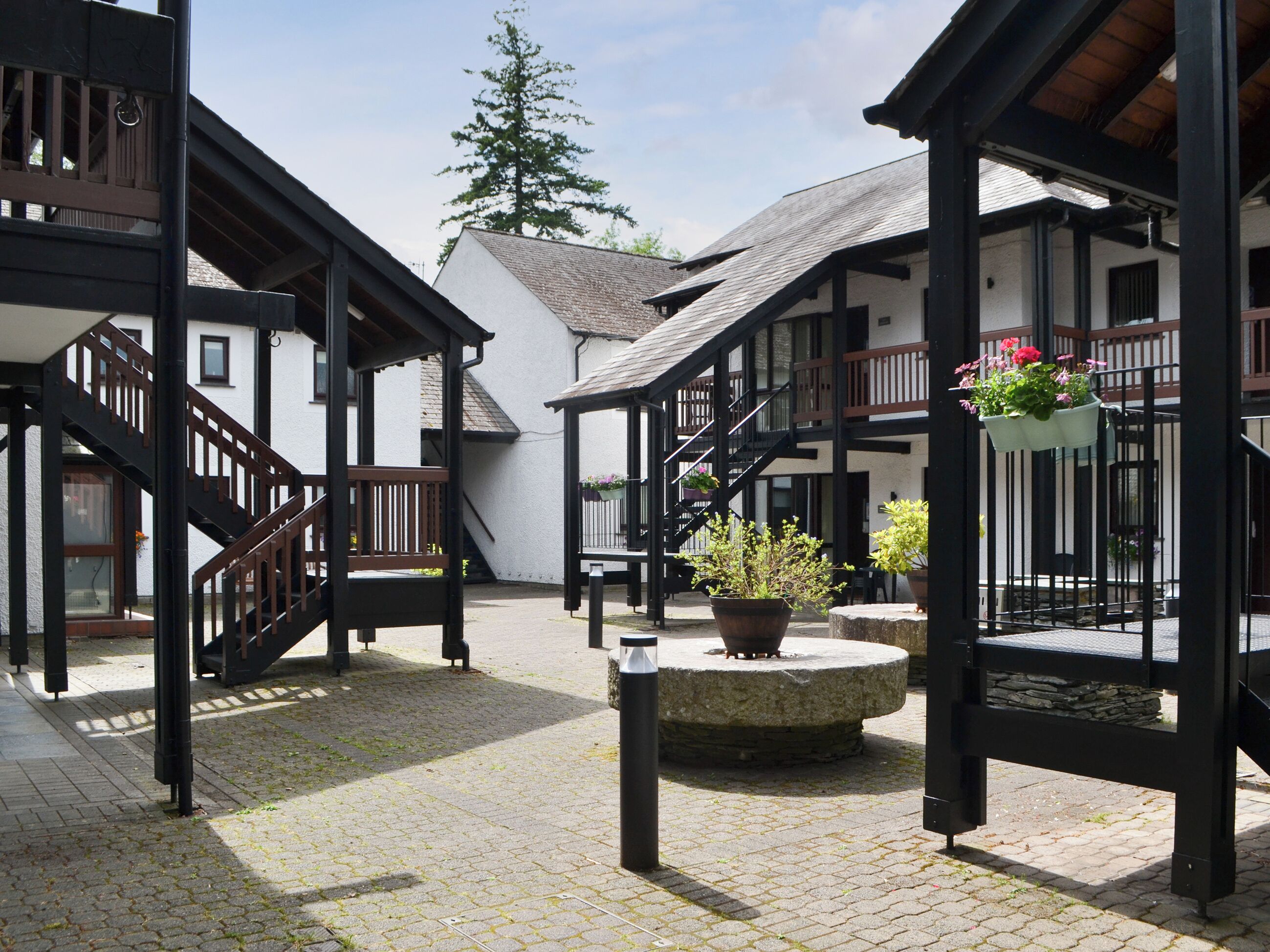 A courtyard with a stone fountain, wooden benches, and a staircase leading to a building with a balcony.