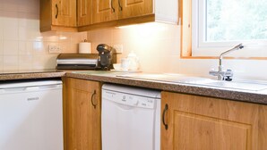 Una cucina con mobili in legno, lavastoviglie integrata, macchina del caffè e finestra sopra il lavello.