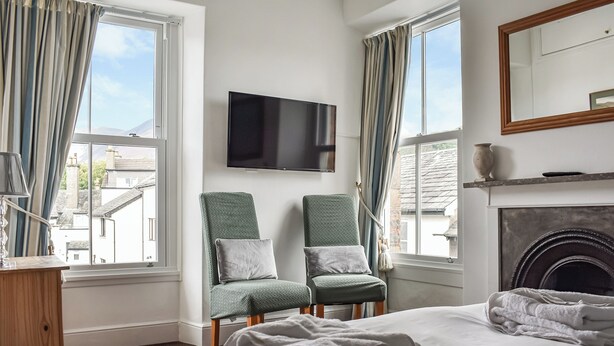 A hotel room with a bed, two chairs, a TV, a fireplace, and curtains. - Pitcairn House-UK41255 (Keswick)