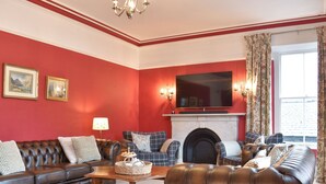 A living room with a fireplace, leather sofas, a wooden coffee table, and a large flat-screen TV mounted above the fireplace. - Pitcairn House-UK41255 (Keswick)