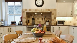 A kitchen with a dining table set for breakfast, including fruits, bread, and condiments. - Pitcairn House-UK41255 (Keswick)