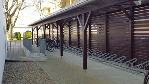 A covered bike parking area with metal bike racks and a gravel path leading to a building. - Excl. Apartment close to the beach, swimming pool, sauna, WLAN, free spa card, max. 3 pers. (Zempin)