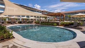 A swimming pool with lounge chairs and umbrellas, surrounded by a building with balconies.