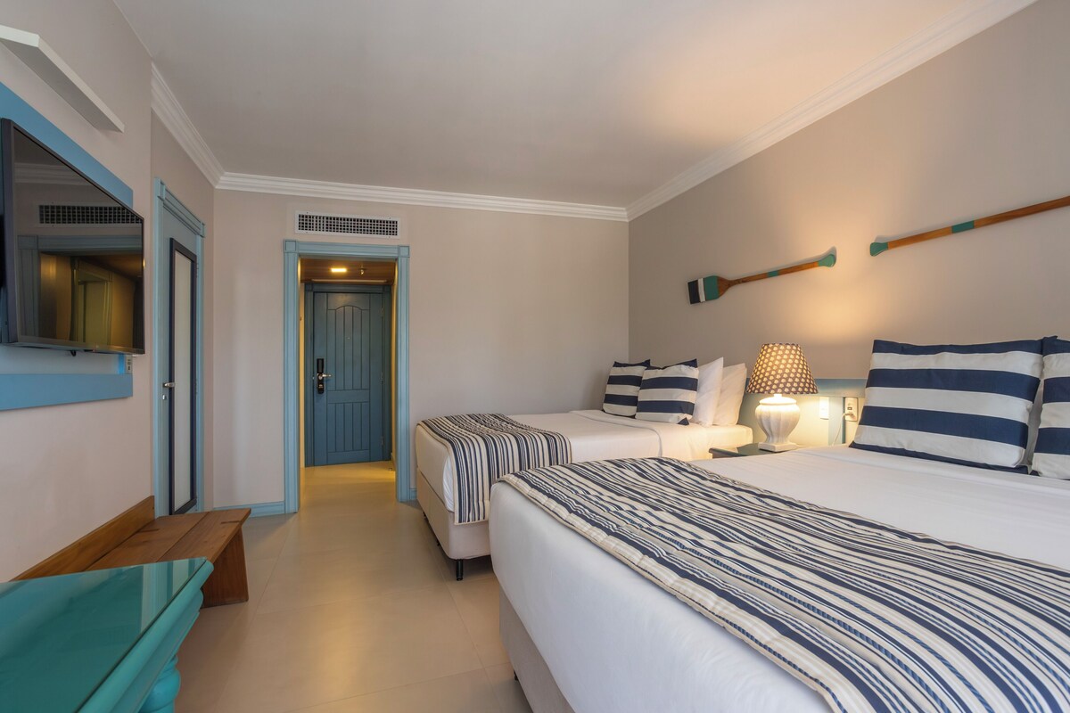 A hotel room with two beds, a bench, a mirror, and a lamp.