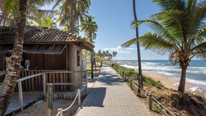 A wooden building with a tiled roof, a paved walkway, and palm trees along a beachside path.