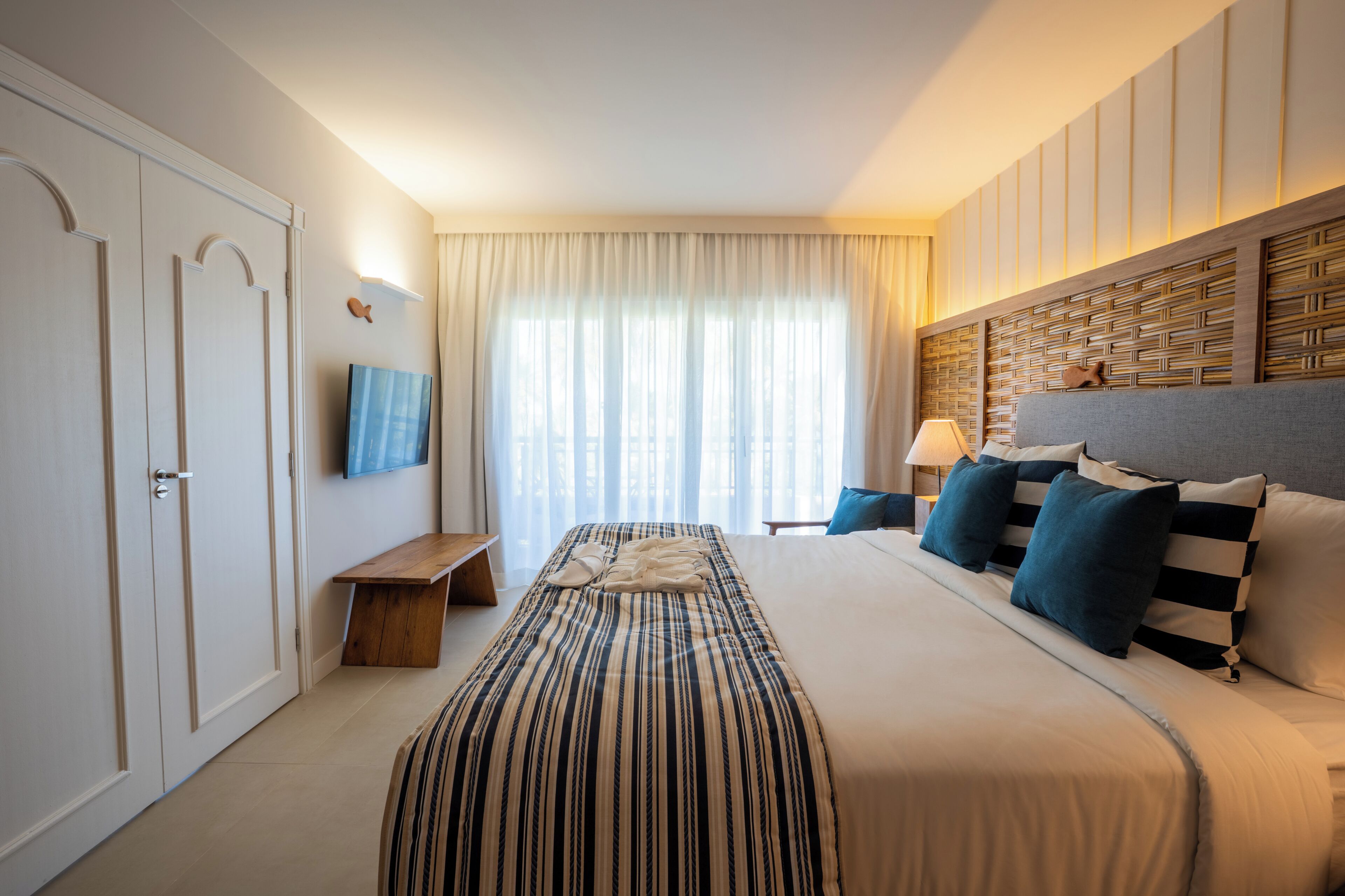 Quarto de hotel com cama, televisão, mesa de cabeceira e janela com cortinas.