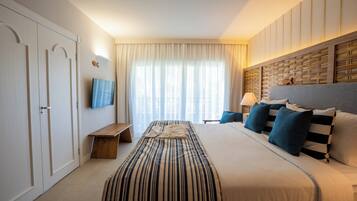 Quarto de hotel com cama, televisão, mesa de cabeceira e janela com cortinas.