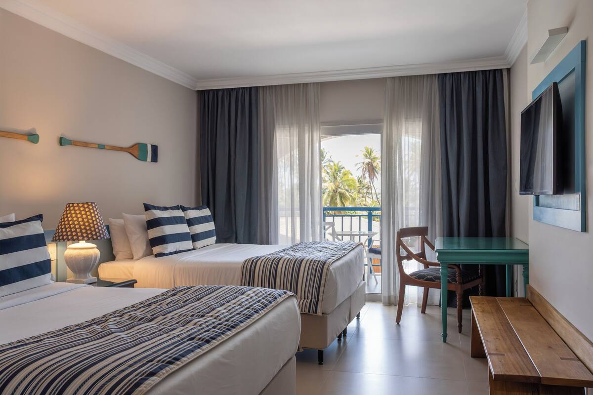 Une chambre d’hôtel avec deux lits, un bureau, une chaise, une télévision et un balcon avec vue.