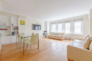 Un salon moderne avec une table à manger en verre, un canapé et un téléviseur fixé au mur.