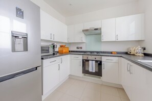 A modern kitchen with white cabinets, a built-in water dispenser, a microwave, a stove, and a kettle. - Spacious and Central 3 Bedroom House in Paddington (London)