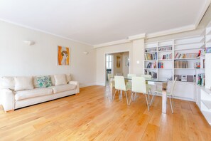 Un salon moderne avec un canapé blanc, une table à manger en verre entourée de chaises et une bibliothèque remplie de livres.