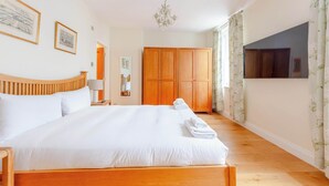 A hotel room with a large bed, wooden wardrobe, a chandelier, and a TV. - Spacious and Central 3 Bedroom House in Paddington (London)
