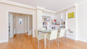 A dining area with a glass table and chairs, a bookshelf, and a hallway leading to a laundry room. - Spacious and Central 3 Bedroom House in Paddington (London)