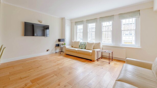 A spacious living room with hardwood flooring, a sofa, a coffee table, and a TV mounted on the wall. - Spacious and Central 3 Bedroom House in Paddington (London)