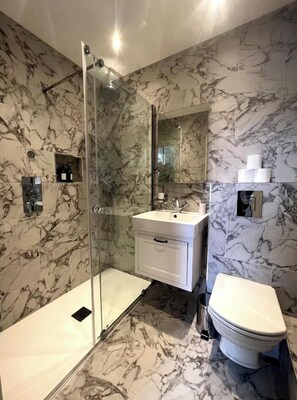 Ein modernes Badezimmer mit Duschabtrennung aus Glas, einem weißen Waschbecken und einer Toilette.