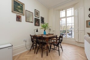 Ein Essbereich mit einem Holztisch und Stühlen, einer Vase mit Blumen sowie gerahmten Kunstwerken an der Wand.