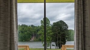 Une pièce dotée d’une grande porte-fenêtre coulissante qui donne sur une terrasse extérieure avec deux chaises en bois et une vue sur un lac et une forêt.