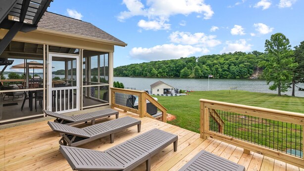 Une terrasse avec des chaises longues donnant sur un lac, un espace abrité avec des tables et une vue sur une zone boisée de l’autre côté de l’eau.