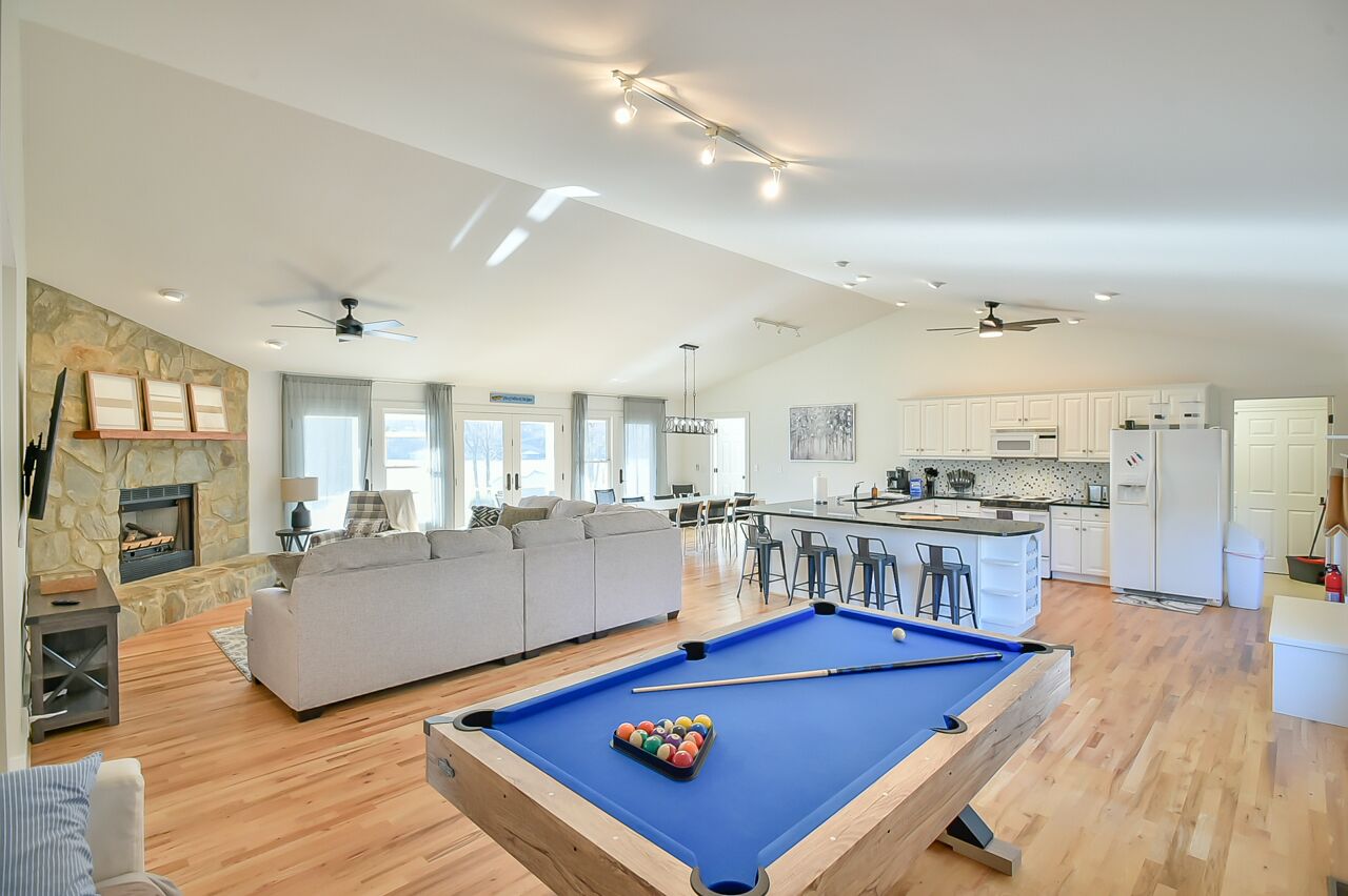 A spacious living area with a pool table, a fireplace, and a kitchen in the background.
