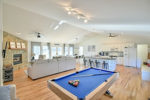 Un salón amplio con mesa de billar, chimenea y cocina al fondo.