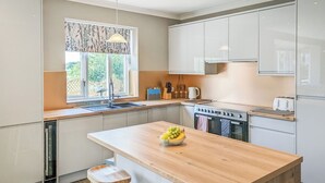 A modern kitchen with a central island, a sink, a stove, and a window with a view of greenery. - 4 bedroom accommodation in Carlton Colville, near Lowestoft (Carlton Colville, near Lowestoft)