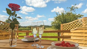 A wooden table with a vase of a single rose, two glasses of champagne, and a bowl of strawberries. - 4 bedroom accommodation in Carlton Colville, near Lowestoft (Carlton Colville, near Lowestoft)