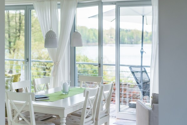 Comedor con mesa, sillas y vistas a un lago a través de amplios ventanales.
