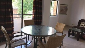 Een kamer met een ronde glazen tafel, omringd door rieten stoelen, een donkere bank en een klein bijzettafeltje.