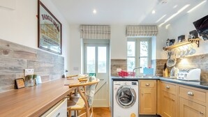 Una cocina moderna con armarios de madera, lavadora integrada y una zona de comedor con mesa y sillas de madera.