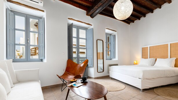 Een moderne slaapkamer met een wit bed, een houten stoel, een klein tafeltje en een grote spiegel.