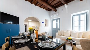 Een eetruimte met een tafel gedekt voor vier personen, een keuken achtergrond en een woonkamer met een bank en een raam.